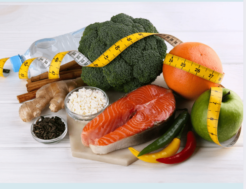 A selection of nutrient-rich foods including salmon, broccoli, fruits, ginger, and cottage cheese wrapped in a measuring tape—ideal components for the Metabolic Confusion Diet and sustainable weight loss.